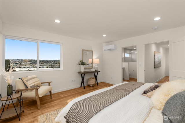 bedroom featuring light wood-type flooring, a wall unit AC, and ensuite bath