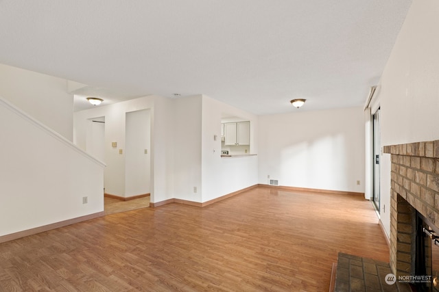 unfurnished living room with light wood finished floors, baseboards, a fireplace, and visible vents