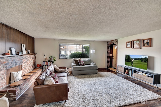 living room with a fireplace, a textured ceiling, dark hardwood / wood-style flooring, and wooden walls