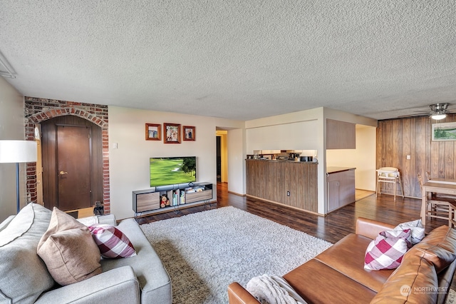 living room featuring a textured ceiling, ceiling fan, wood walls, and dark hardwood / wood-style floors