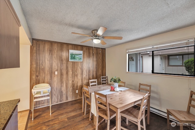 dining space with a textured ceiling, dark hardwood / wood-style floors, ceiling fan, and wood walls