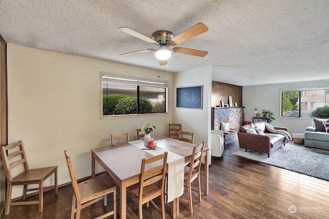 dining space featuring a fireplace, a textured ceiling, ceiling fan, and dark wood-type flooring