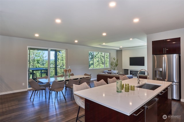 kitchen with dark wood-type flooring, sink, an island with sink, a kitchen bar, and stainless steel appliances