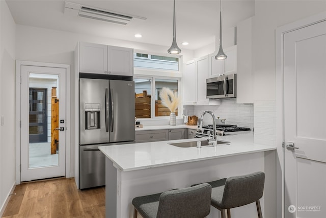 kitchen with kitchen peninsula, stainless steel appliances, sink, pendant lighting, and white cabinets