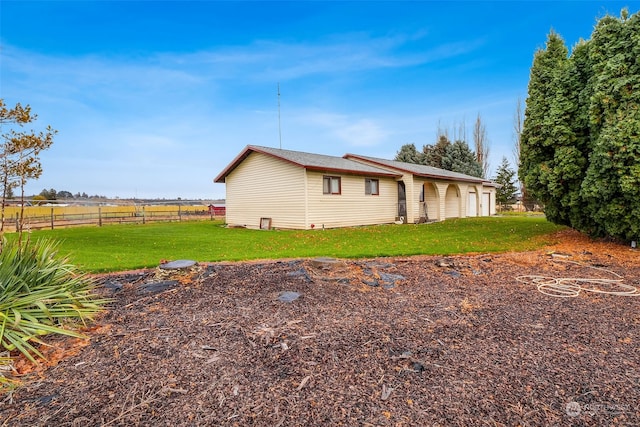 view of side of property featuring a rural view, a garage, and a lawn