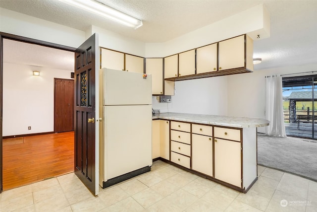 kitchen featuring a textured ceiling, white refrigerator, light hardwood / wood-style floors, and kitchen peninsula