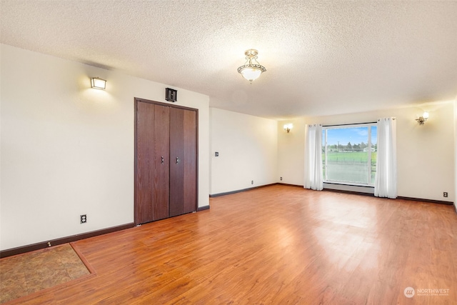 empty room with a baseboard radiator, light hardwood / wood-style floors, and a textured ceiling