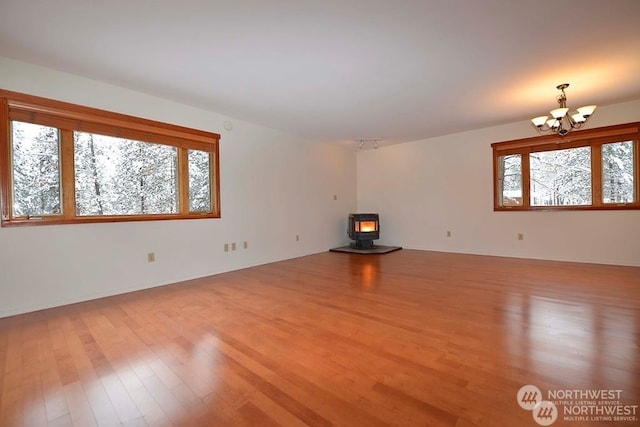 unfurnished living room featuring an inviting chandelier, a wood stove, and light hardwood / wood-style flooring