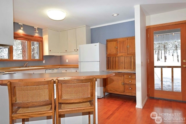 kitchen with decorative backsplash, white appliances, ornamental molding, light hardwood / wood-style flooring, and sink