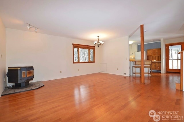 unfurnished living room with an inviting chandelier, a wood stove, and wood-type flooring