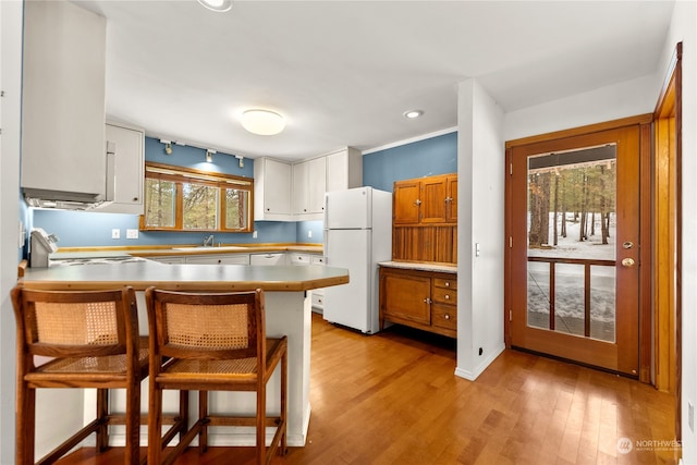 kitchen featuring a kitchen bar, kitchen peninsula, white appliances, a wealth of natural light, and white cabinets