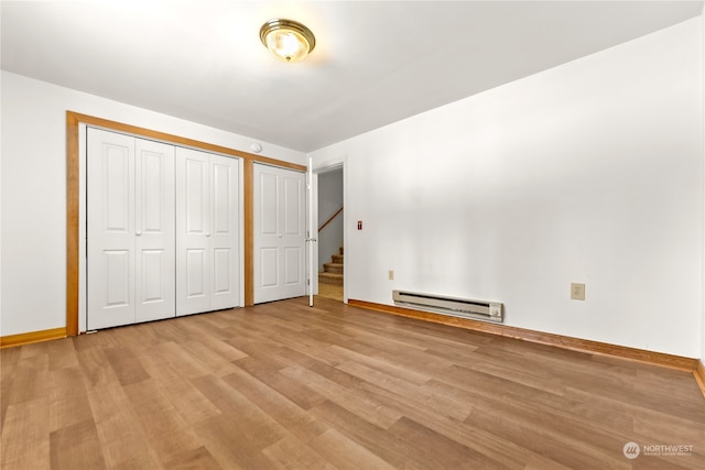 unfurnished bedroom with baseboard heating, two closets, and light hardwood / wood-style flooring