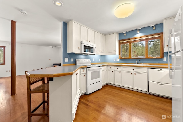 kitchen with white appliances, white cabinetry, sink, kitchen peninsula, and a breakfast bar area