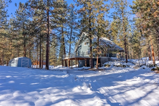 yard layered in snow featuring a wooden deck and a shed