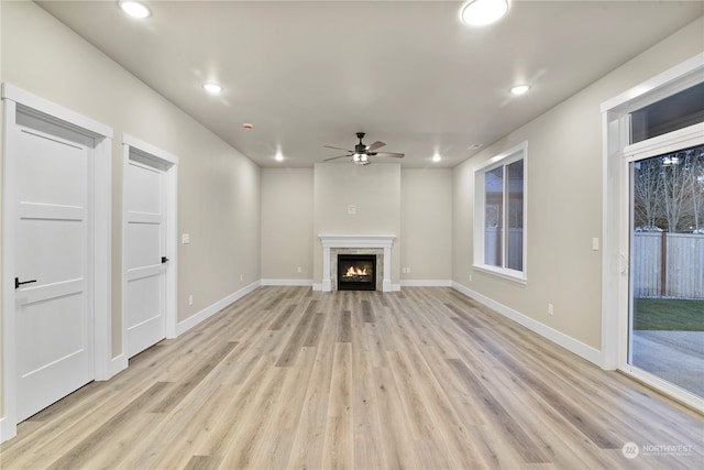 unfurnished living room with ceiling fan, a fireplace, and light hardwood / wood-style floors