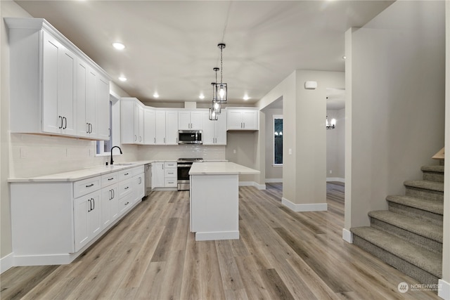 kitchen with a center island, white cabinets, sink, appliances with stainless steel finishes, and decorative light fixtures