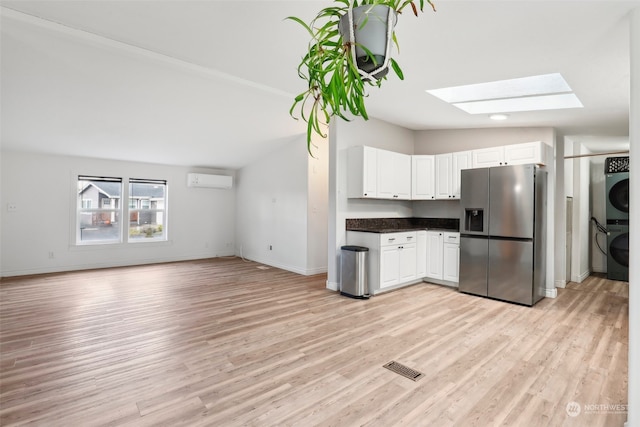 kitchen with vaulted ceiling with skylight, light hardwood / wood-style floors, stainless steel refrigerator with ice dispenser, and stacked washer and clothes dryer