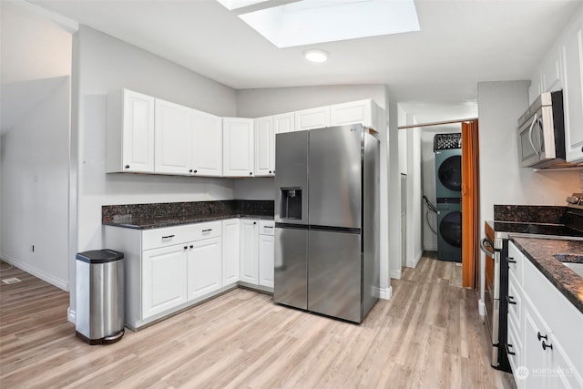 kitchen with stainless steel appliances, lofted ceiling with skylight, stacked washer and clothes dryer, white cabinets, and light hardwood / wood-style floors