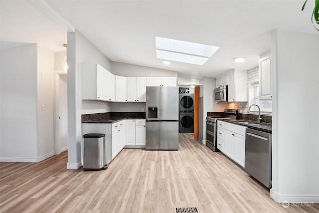 kitchen featuring white cabinetry, sink, stacked washing maching and dryer, stainless steel appliances, and light wood-type flooring