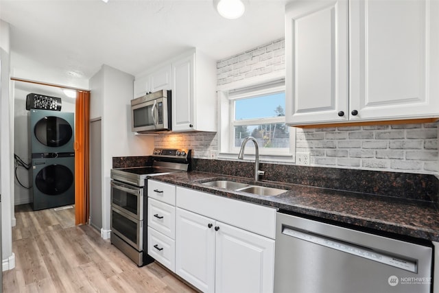 kitchen with sink, stacked washer and dryer, light hardwood / wood-style floors, white cabinetry, and stainless steel appliances