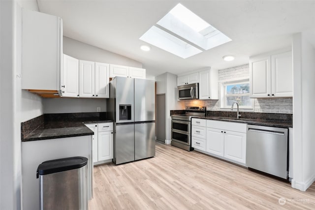 kitchen with light hardwood / wood-style flooring, lofted ceiling with skylight, decorative backsplash, white cabinets, and appliances with stainless steel finishes