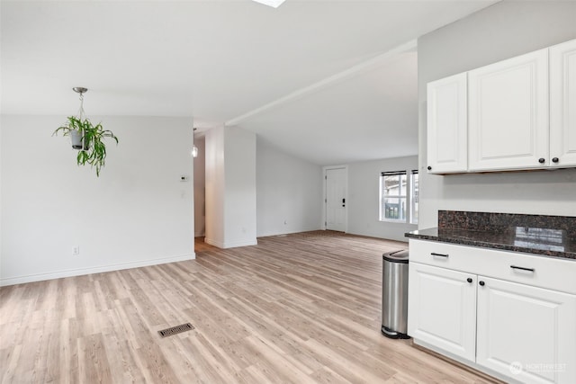 kitchen with lofted ceiling, white cabinetry, light wood-type flooring, and dark stone counters