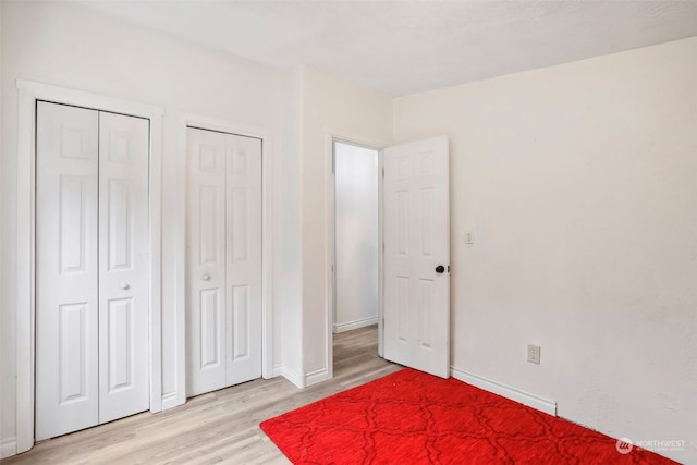 unfurnished bedroom featuring multiple closets and light wood-type flooring