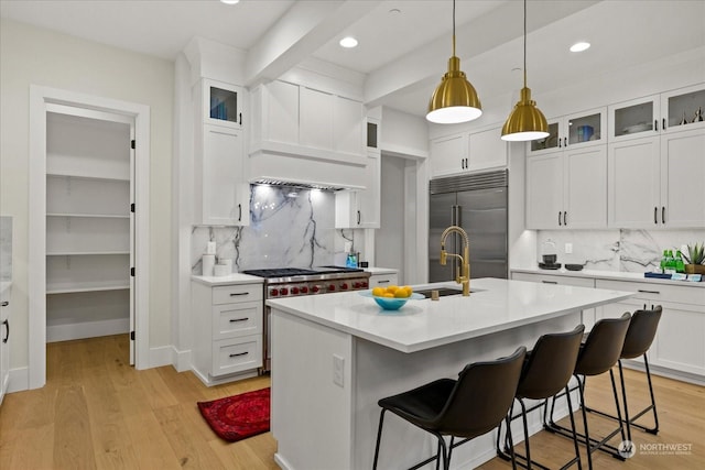 kitchen featuring a center island with sink, premium appliances, white cabinets, and tasteful backsplash