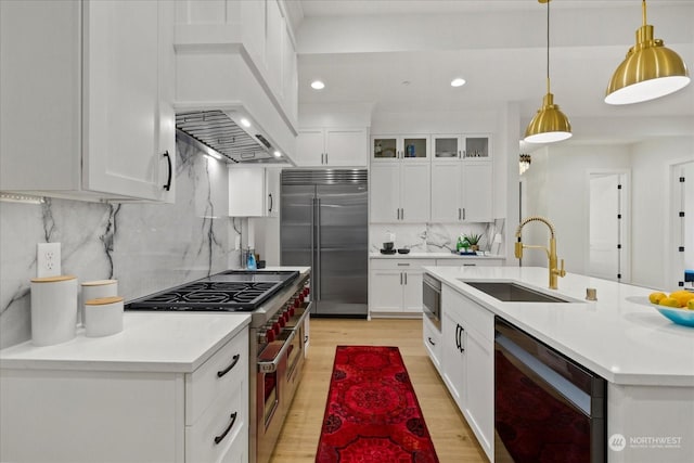 kitchen featuring built in appliances, sink, white cabinets, and decorative light fixtures