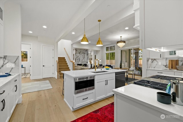 kitchen with appliances with stainless steel finishes, sink, light hardwood / wood-style flooring, white cabinets, and hanging light fixtures