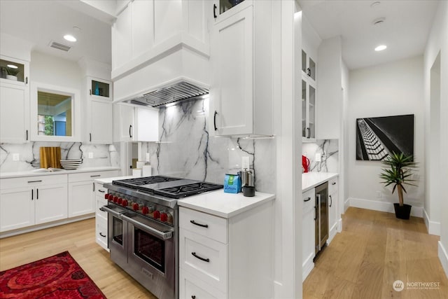 kitchen featuring light hardwood / wood-style floors, range with two ovens, white cabinetry, and backsplash