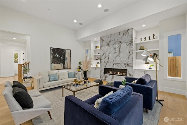 living room featuring a high end fireplace, built in shelves, and light hardwood / wood-style flooring