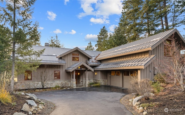 view of front of home with driveway, a standing seam roof, stone siding, and board and batten siding