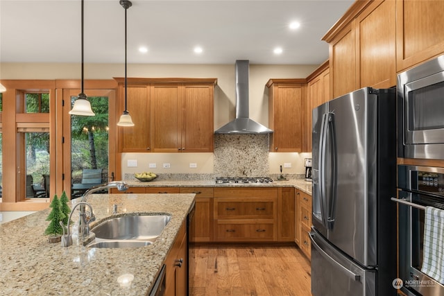 kitchen with appliances with stainless steel finishes, light stone counters, decorative light fixtures, wall chimney range hood, and a sink