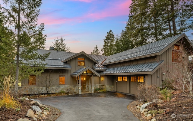 view of front of property with board and batten siding, a standing seam roof, driveway, and stone siding