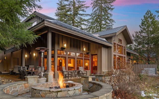 rear view of house featuring a standing seam roof, metal roof, a fire pit, board and batten siding, and a chimney