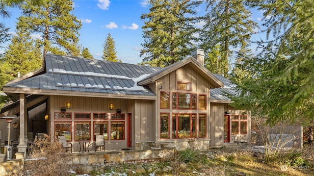 back of property featuring metal roof, a standing seam roof, a chimney, and board and batten siding