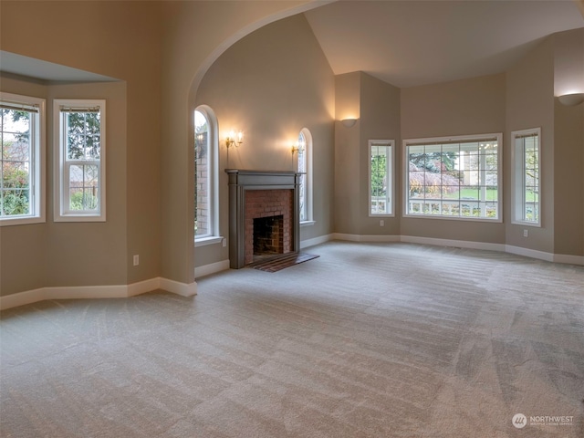 unfurnished living room featuring high vaulted ceiling, light colored carpet, and a brick fireplace