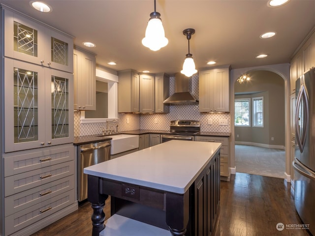 kitchen with gray cabinetry, wall chimney range hood, pendant lighting, a kitchen island, and appliances with stainless steel finishes