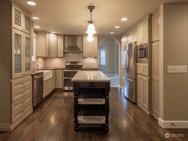 kitchen featuring sink, wall chimney exhaust hood, stainless steel appliances, tasteful backsplash, and pendant lighting