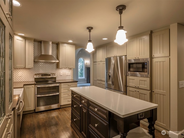 kitchen with wall chimney range hood, tasteful backsplash, dark hardwood / wood-style flooring, decorative light fixtures, and appliances with stainless steel finishes