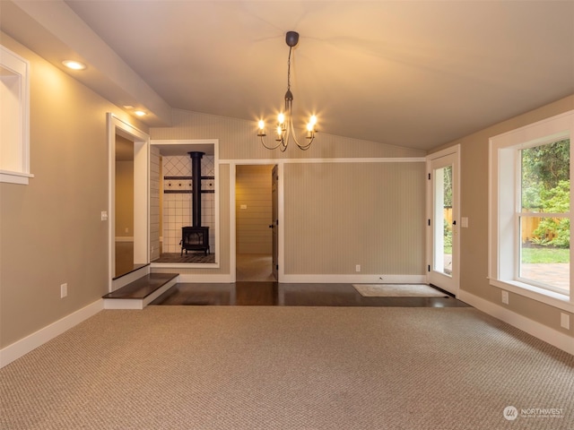 interior space with a chandelier, a wood stove, vaulted ceiling, and dark carpet