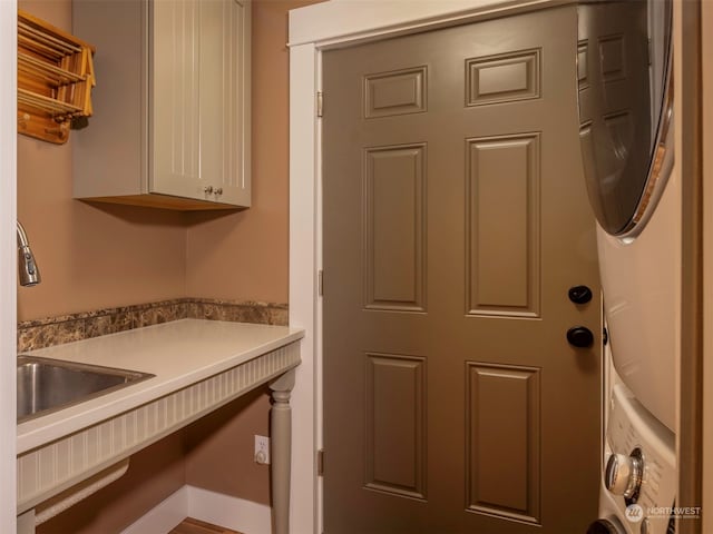 laundry room featuring cabinets, stacked washing maching and dryer, and sink