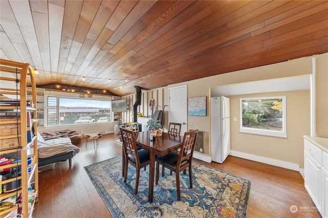 dining area with wood-type flooring, wooden ceiling, a wealth of natural light, and a wood stove