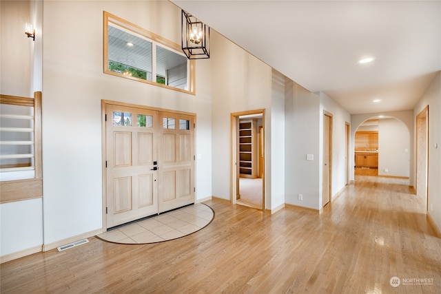 foyer entrance with light hardwood / wood-style flooring, a towering ceiling, and a notable chandelier