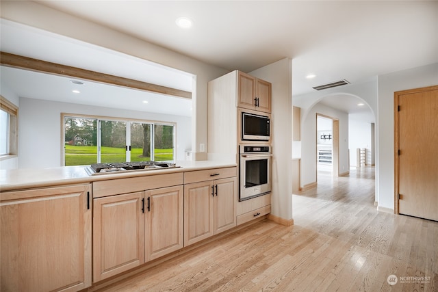 kitchen featuring beamed ceiling, light brown cabinets, light wood-type flooring, and stainless steel appliances