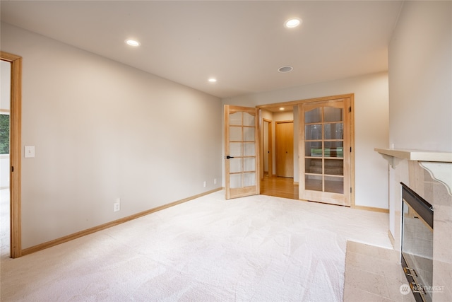 unfurnished living room with a tile fireplace, light carpet, and french doors