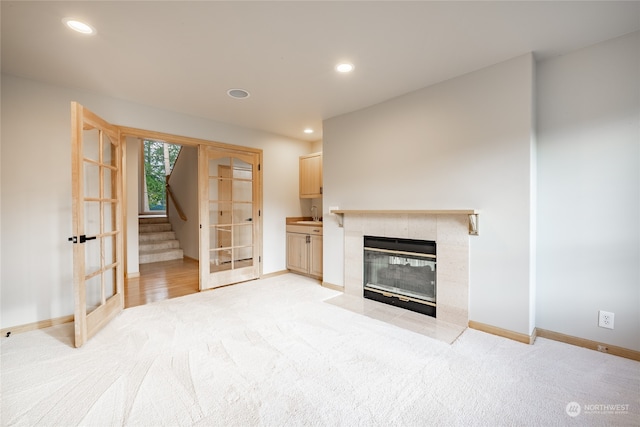 unfurnished living room with sink, light carpet, a tile fireplace, and french doors