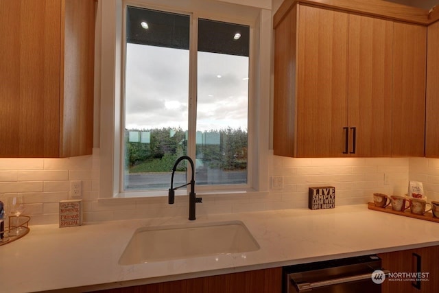 kitchen with dishwashing machine, light stone counters, decorative backsplash, and sink