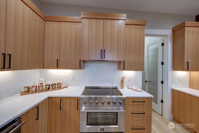 kitchen with light brown cabinetry, light wood-type flooring, backsplash, high end stove, and dishwasher